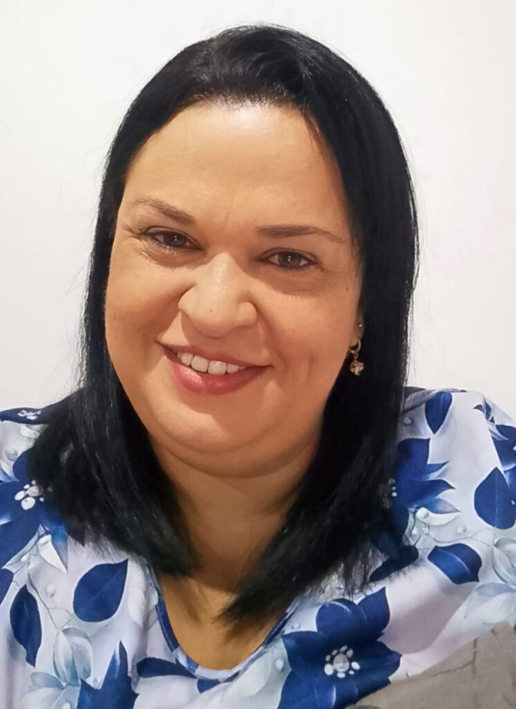 Pessoa sentada em ambiente interno, olhando para a câmera, vestindo roupa com estampa floral.