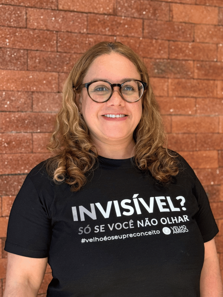 Retrato da autora do artigo em frente a uma parede de tijolos, utilizando camiseta de campanha do Instituto Velho Amigo.