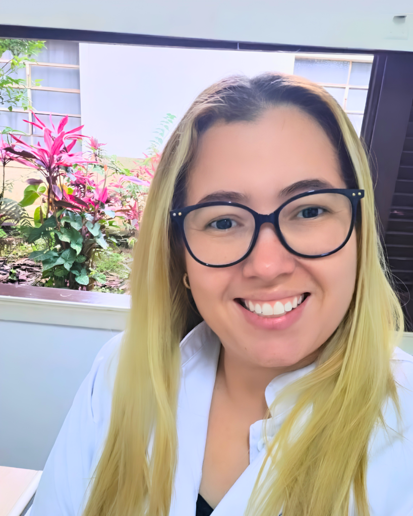 Retrato da autora do artigo em ambiente interno da instituição, com vegetação visível ao fundo.